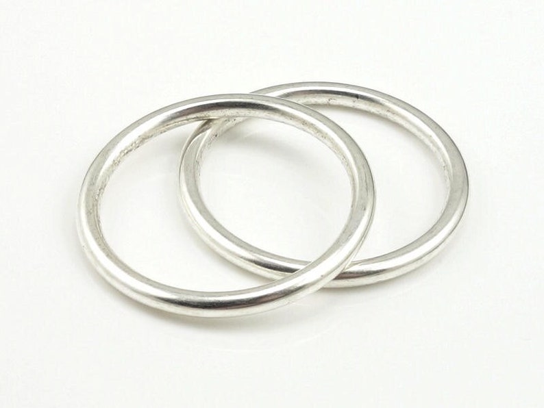 May include: Two silver rings, one slightly larger than the other, are interlocked. The rings are smooth and have a polished finish.