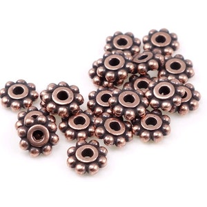 May include: A group of 15 copper-coloured metal beads with a flower-shaped design. Each bead has a small hole in the centre.
