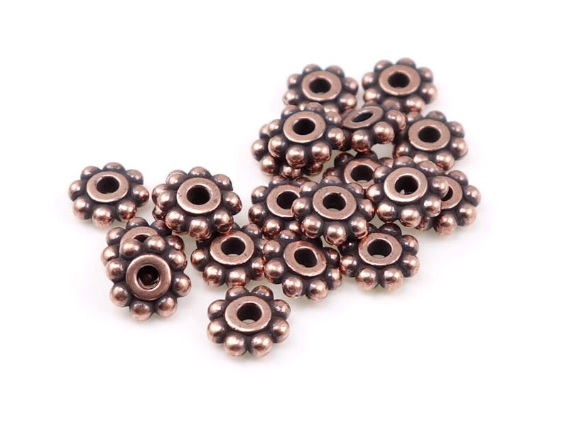 May include: A group of 15 copper-coloured metal beads with a flower-shaped design. Each bead has a small hole in the centre.