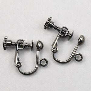 May include: Two silver-toned clip-on earring findings. Each finding has a screw mechanism, a curved lever, and a small, round decorative element. The earrings are designed for non-pierced ears and are displayed on a white surface.