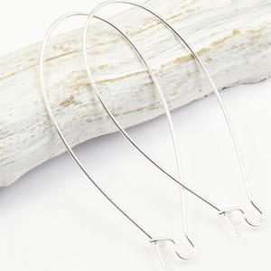 May include: Two silver earring hoops with a slightly oval shape. The hoops are made of thin wire and have a simple, elegant design.