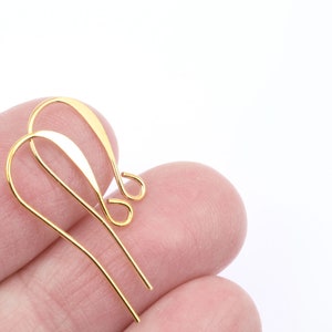 Puede incluir: Dos ganchos para pendientes de color dorado, tambi&eacute;n conocidos como alambres para orejas, se sostienen en una mano. Los ganchos son de metal y tienen un acabado liso y brillante.