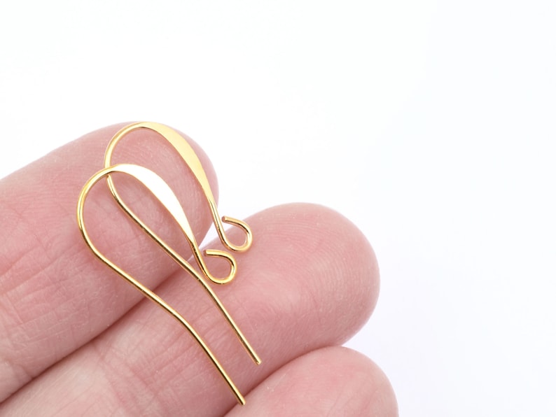 Puede incluir: Dos ganchos para pendientes de color dorado, tambi&eacute;n conocidos como alambres para orejas, se sostienen en una mano. Los ganchos son de metal y tienen un acabado liso y brillante.