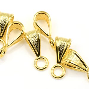 May include: Four gold-tone metal pendant bails with a textured finish. Each bail has a loop at the top and a smaller loop at the bottom.