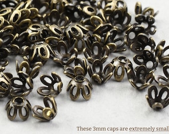 May include: A close-up of a pile of small, antique gold-coloured metal bead caps. The caps are shaped like a flower with five petals. These 3mm caps are extremely small!