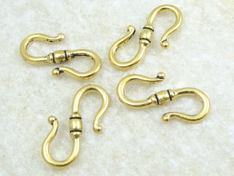 May include: Five gold-toned metal lobster clasps with black accents. The clasps are designed with a curved shape and a small bead in the center.