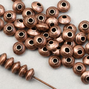 May include: A pile of copper-colored metal beads with a hole in the center. The beads are round and have a slightly domed shape. A strand of the beads is strung on a thin wire.