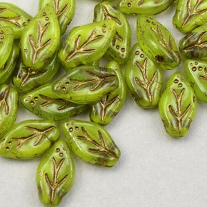 May include: A collection of green glass beads with gold leaf accents in the shape of leaves.