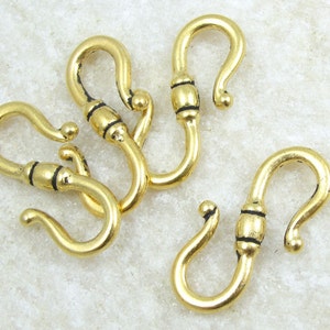 May include: Four gold-toned metal hooks with black accents. The hooks are designed with a curved shape and a small loop at the top.