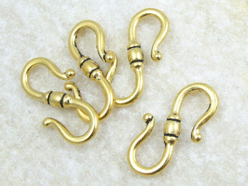 May include: Four gold-toned metal hooks with black accents. The hooks are designed with a curved shape and a small loop at the top.
