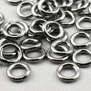 May include: A pile of black metal jump rings. The rings are all the same size and are arranged in a random pattern.