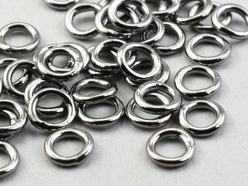 May include: A pile of black metal jump rings. The rings are all the same size and are arranged in a random pattern.