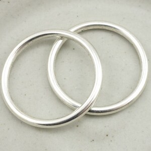 May include: Two silver jump rings, one slightly larger than the other, are interlocked. The rings are smooth and shiny.