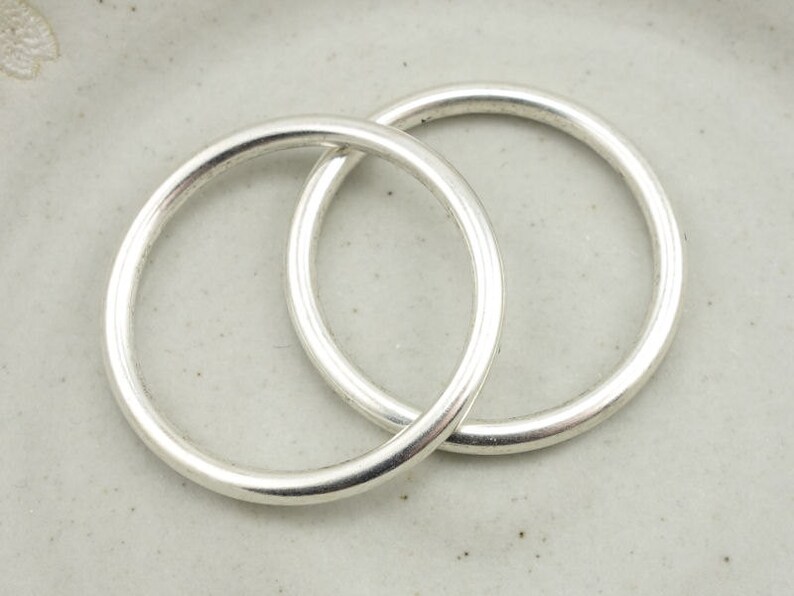 May include: Two silver jump rings, one slightly larger than the other, are interlocked. The rings are smooth and shiny.