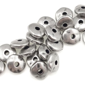 May include: A pile of silver-toned metal beads with a slightly irregular, rounded shape. Each bead has a hole in the center.