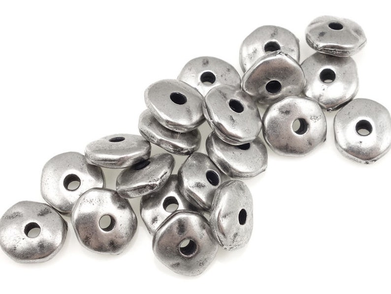 May include: A pile of silver-toned metal beads with a slightly irregular, rounded shape. Each bead has a hole in the center.