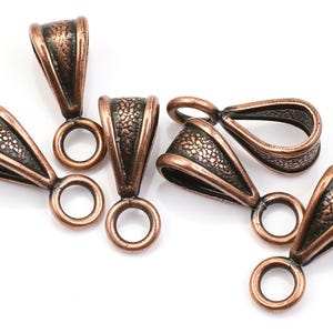 May include: Six copper-toned metal pendant bails with a textured finish. Each bail has a loop at the top and a smaller loop at the bottom.