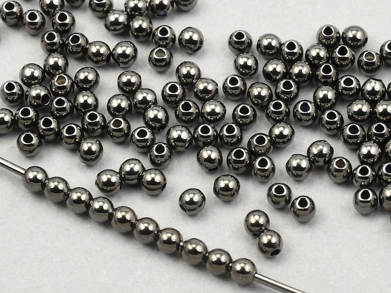 May include: A collection of small, shiny, silver-colored metal beads. Some beads are strung on a wire, while others are scattered. The beads have a smooth, reflective surface and a hole through the center.
