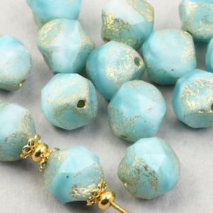 May include: Light blue faceted beads with gold accents. The beads have a slightly irregular shape and are strung on a gold-colored wire. The beads are a pale turquoise color with gold flecks.