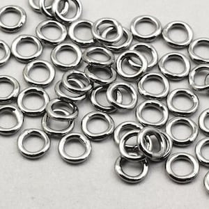 May include: A large pile of silver jump rings. The rings are all the same size and are arranged in a random pattern.