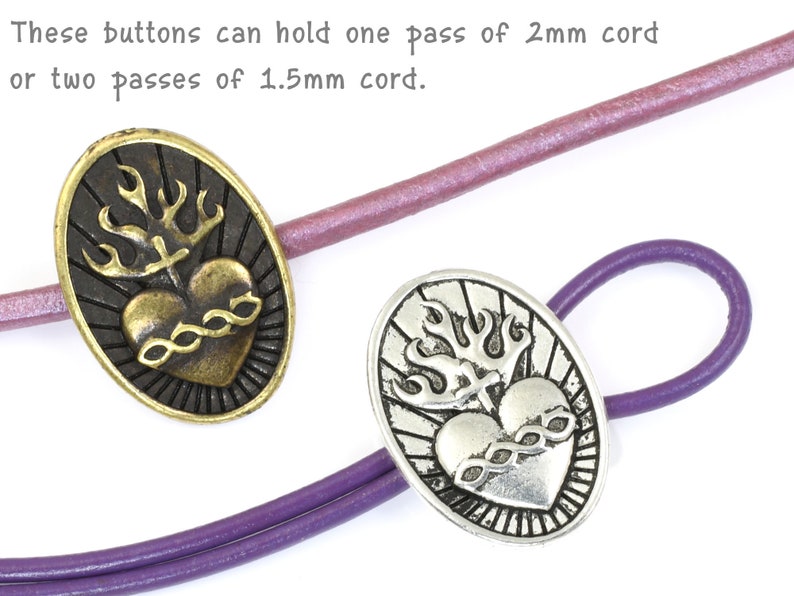 May include: Two oval-shaped metal buttons with a heart and flame design. The button on the left is gold-toned and the button on the right is silver-toned.  The text on the image reads: "These buttons can hold one pass of 2mm cord or two passes of 1.5mm cord."