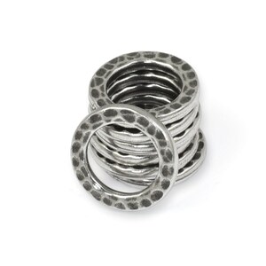 May include: A stack of silver-colored metal rings with a hammered texture. The rings are circular with a slightly irregular surface, creating a rustic or industrial aesthetic. The rings are stacked on a white background.