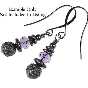 May include: A pair of dangle earrings with black metal wire and beads. The earrings feature a purple crystal bead and a black metal bead with a textured surface.