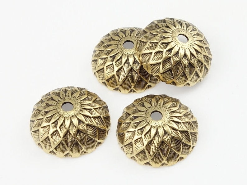 May include: Four gold-toned metal decorative caps with a floral design. Each cap has a small hole in the center.
