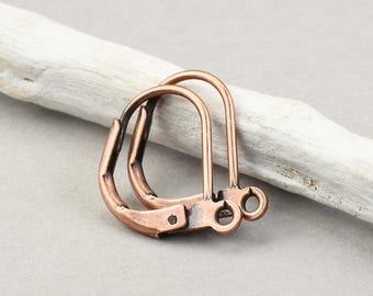 May include: A pair of copper-toned metal leverback earring findings featuring a curved wire loop and a small circular attachment ring at the base for jewellery making, showcasing a weathered metallic finish with dark oxidation in the crevices.