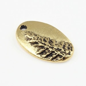 May include: Gold-toned oval charm with a raised design of a sprig of leaves. The charm has a small hole at the top for attaching to a necklace or bracelet.