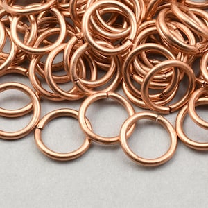 May include: A pile of small, copper-colored jump rings. The rings are all the same size and are arranged in a random pattern.