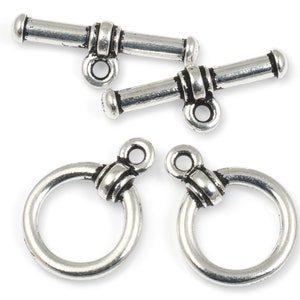 May include: Two silver toggle clasps with a ring on each end. The clasps are designed with a decorative knot and a small loop.