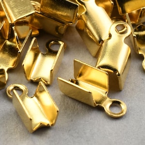 May include: A close-up of a pile of gold-colored metal clasps with a loop on one end. The clasps are designed to be used for jewelry making.