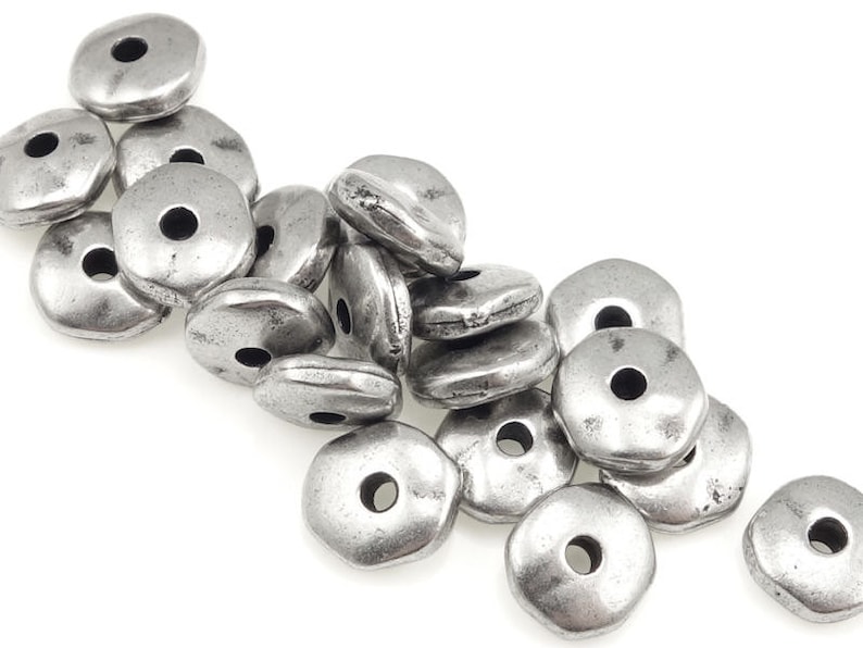May include: A pile of silver-toned metal beads with a hexagonal shape and a hole in the center. The beads are scattered on a white background.