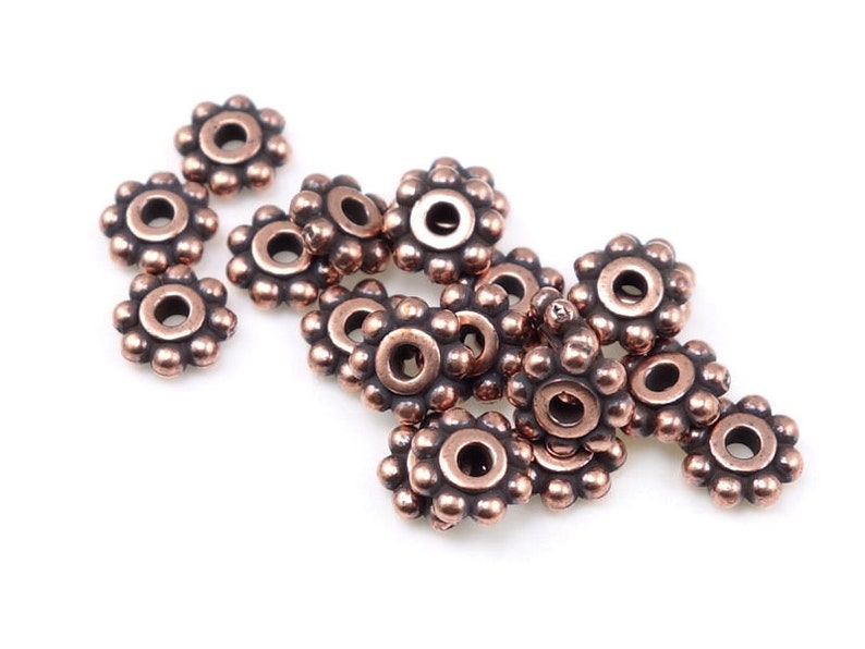 May include: A group of 14 copper-coloured metal beads with a flower-shaped design. Each bead has a small hole in the centre.