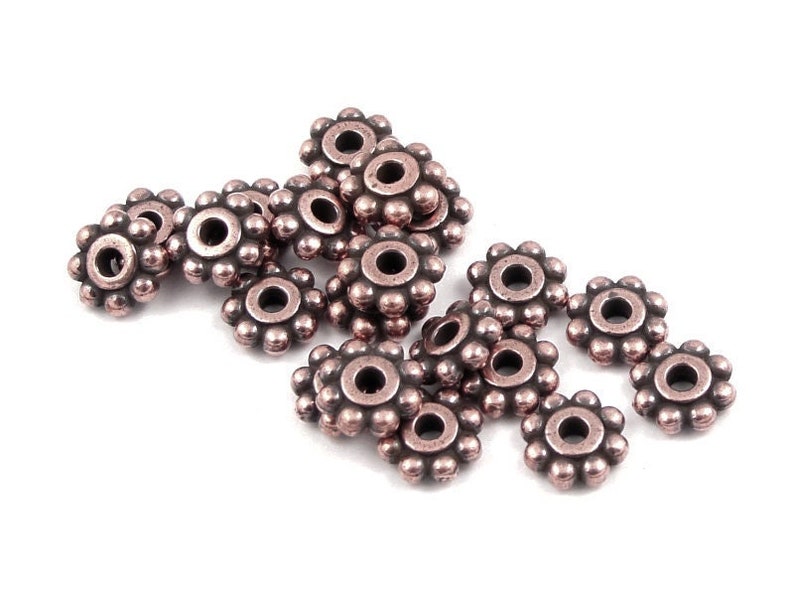 May include: A group of 14 copper-coloured metal bead caps with a decorative flower design. The bead caps are arranged in a loose pile on a white background.