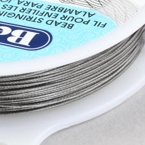 May include: A spool of silver-colored bead stringing wire. The label reads "Bead Stringing Wire, Fil Pour Enfiler Les Alambre Para"