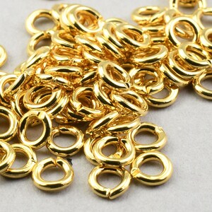May include: A pile of gold-colored jump rings, a type of jewelry finding used for connecting chains, cords, and other jewelry components.