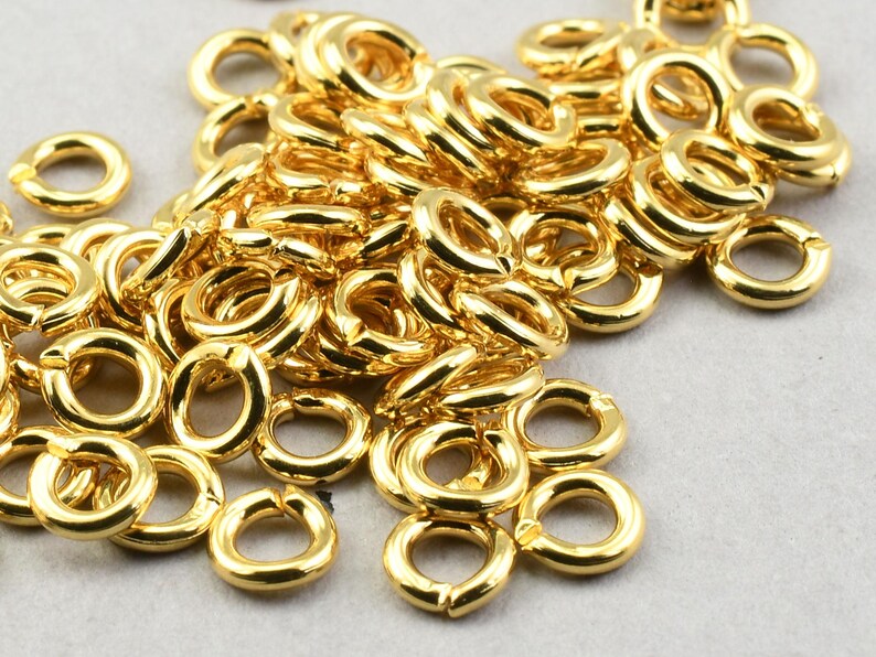 May include: A pile of gold-colored jump rings, a type of jewelry finding used for connecting chains, cords, and other jewelry components.