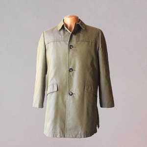 May include: A vintage olive green coat with a collared neckline and three black buttons. The coat has two front pockets and a tailored fit. The coat is displayed on a mannequin against a neutral background.