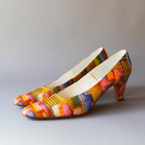 May include: A pair of patterned court shoes with a low heel. The shoes have a patchwork design in yellow, pink, orange, and blue. The heels are approximately 5 cm high. The interior is white.