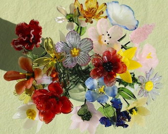 May include: A colorful bouquet of glass flowers in various shapes and sizes. The flowers are in shades of red, yellow, blue, pink, and orange, with green stems and leaves. The arrangement is in a clear glass vase.