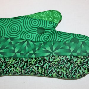 May include: Green oven mitt with a geometric pattern. The mitt is made of fabric and has a loop for hanging.