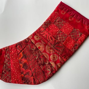 May include: Red and gold Christmas stocking with a patchwork design. The stocking is made of different fabrics with various patterns, including circles, stars, and geometric shapes.