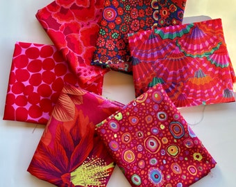May include: Six different fabric swatches in various shades of red with different patterns. The patterns include polka dots, floral, geometric, and abstract designs.