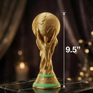 May include: A gold-colored FIFA World Cup trophy replica featuring a figure holding up a globe, standing on a base with a green band and the text FIFA WORLD CUP. A vertical line with arrows indicates a total height of 9.5 inches for the trophy.