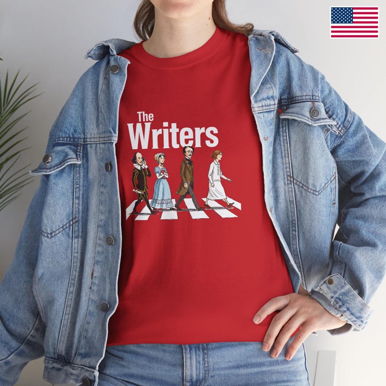 Puede incluir: Camiseta roja con la frase "The Writers" y una ilustraci&oacute;n de escritores famosos cruzando un paso de cebra. Los escritores incluyen a William Shakespeare y Jane Austen. La camiseta se lleva con una chaqueta vaquera azul.