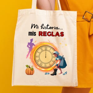 May include: Cream tote bag with the Spanish text "Mi historia... mis REGLAS". The design includes a clock, a pumpkin, a silhouette of a person, and a cartoon illustration of a person wearing a blue dress and a black boot.