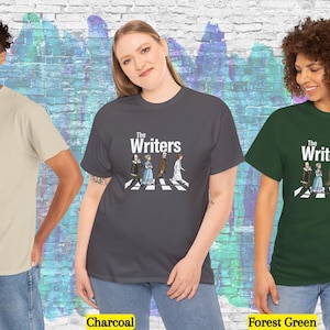 Puede incluir: Camisetas en arena, carb&oacute;n y verde bosque, cada una con el texto "The Writers" sobre una ilustraci&oacute;n de figuras literarias cruzando un paso de cebra. Las camisetas son modeladas por tres personas.