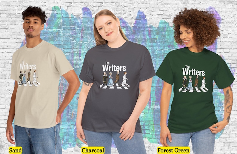 Puede incluir: Camisetas en arena, carb&oacute;n y verde bosque, cada una con el texto "The Writers" sobre una ilustraci&oacute;n de figuras literarias cruzando un paso de cebra. Las camisetas son modeladas por tres personas.